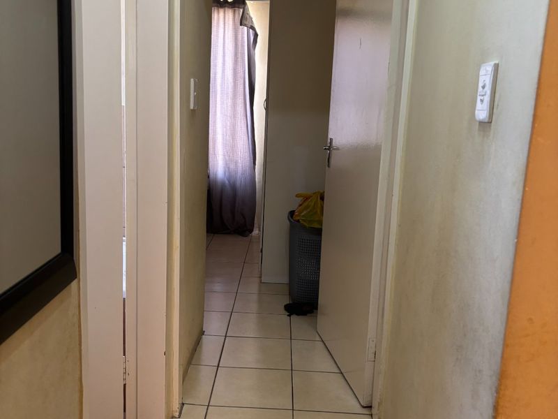 A narrow interior hallway featuring tiled flooring and access to adjacent rooms, showing signs of wear on the wall surfaces.