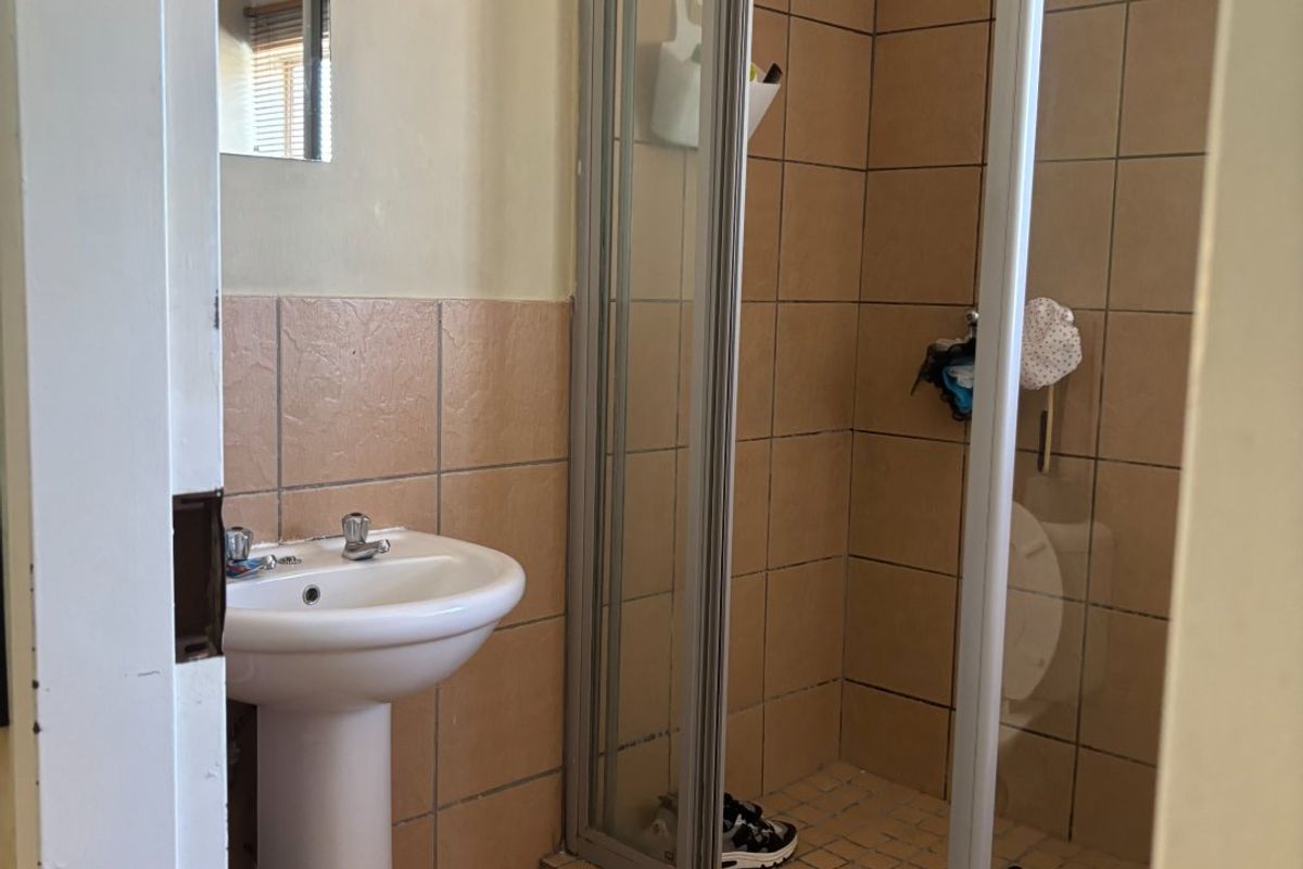 A compact bathroom featuring a pedestal basin and a shower enclosure with tiled walls and flooring, requiring cosmetic updates to modernize the space.