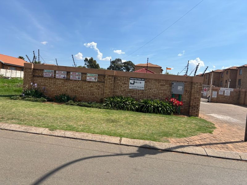 Front view of the apartment complex featuring a secure brick boundary wall with electric fencing and gated access.