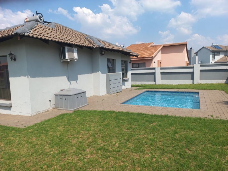 Rear exterior view featuring a swimming pool, paved patio area, and a private garden enclosed by a perimeter wall.