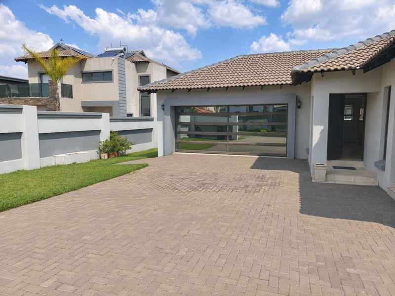 Front exterior view of the property featuring a paved driveway, modern sectional garage door, and a well-maintained boundary wall.