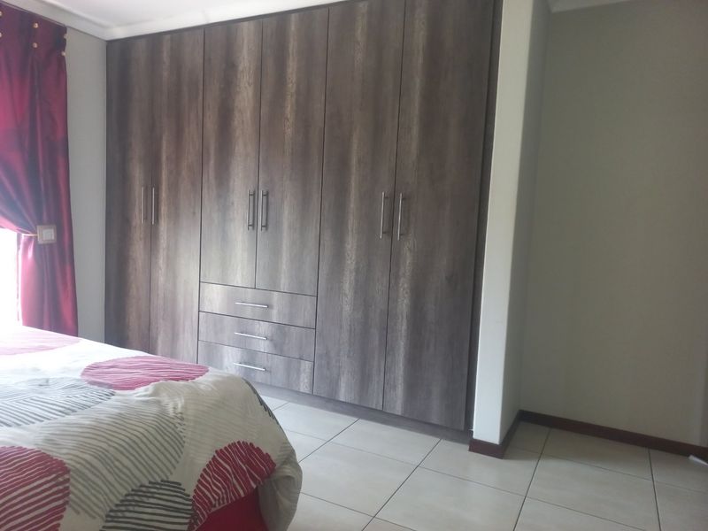 A bedroom featuring modern wood-finish built-in cupboards and neutral tiled flooring.