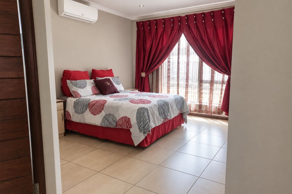 A well-maintained bedroom featuring tiled flooring, recessed downlighting, and a wall-mounted split-system air conditioner, with access to a private balcony through sliding glass doors.