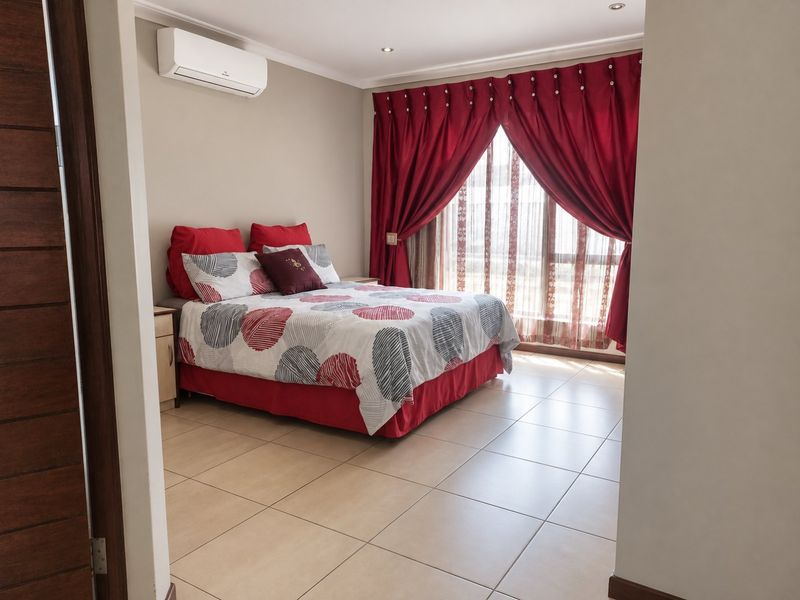 A well-maintained bedroom featuring tiled flooring, recessed downlighting, and a wall-mounted split-system air conditioner, with access to a private balcony through sliding glass doors.