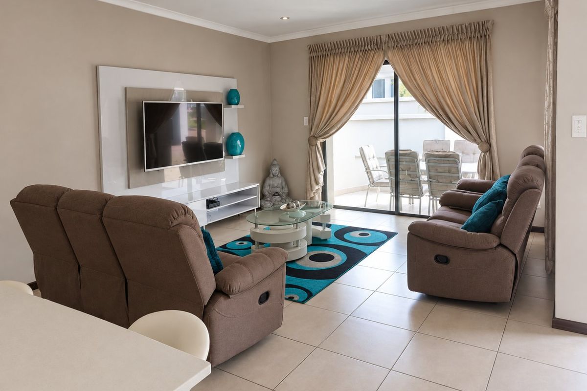 A well-maintained living room featuring tiled flooring, recessed lighting, and a built-in media wall, with direct access to an outdoor patio area.