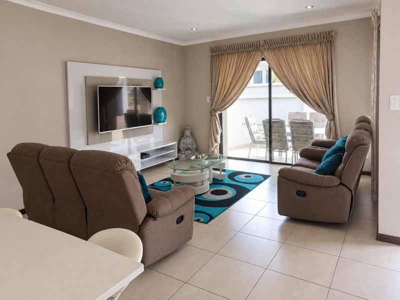 A well-maintained living room featuring tiled flooring, recessed lighting, and a built-in media wall, with direct access to an outdoor patio area.