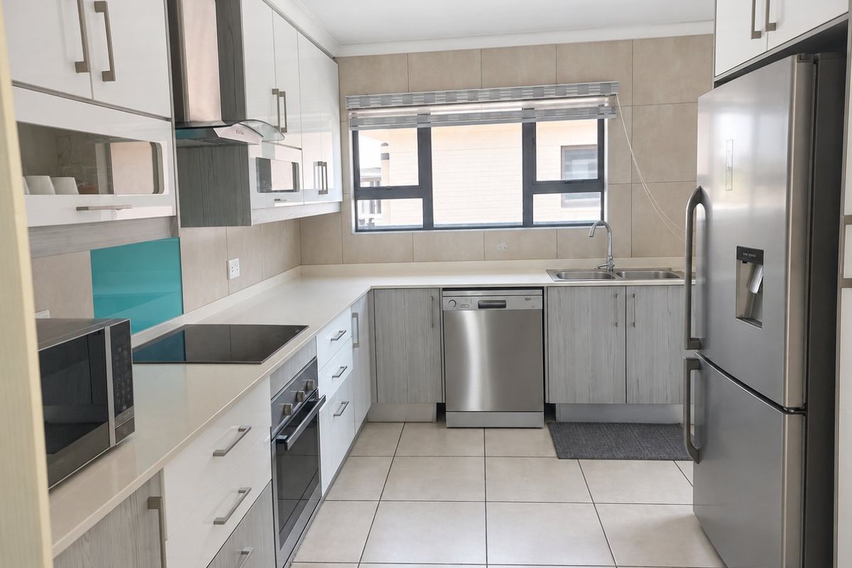 Modern kitchen featuring sleek white and wood-grain cabinetry, stone countertops, integrated appliances, and neutral tiled flooring with ample natural light.