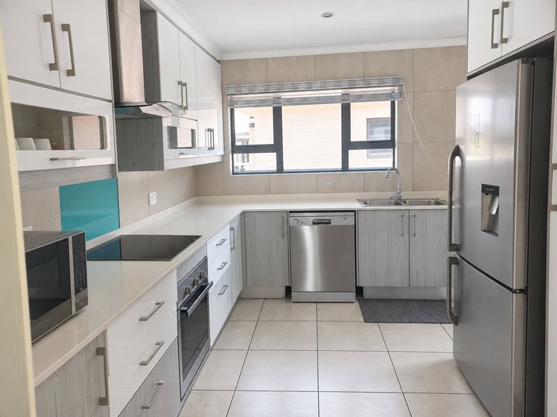 Modern kitchen featuring sleek white and wood-grain cabinetry, stone countertops, integrated appliances, and neutral tiled flooring with ample natural light.