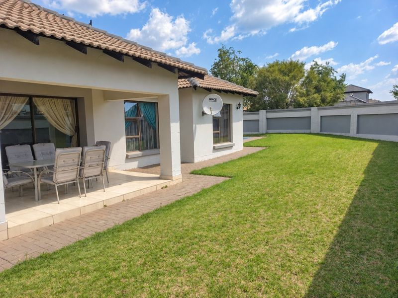 Rear view of the property featuring a covered patio, paved walkway, well-maintained lawn, and secure boundary wall.