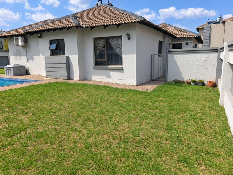 Rear exterior view featuring a private swimming pool, paved patio area, and a well-maintained lawn enclosed by a boundary wall.