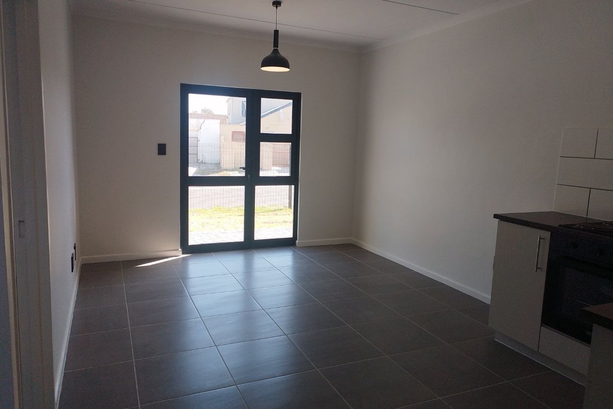 An open-plan living and kitchen area featuring modern tiled flooring, built-in kitchen cabinetry with integrated appliances, and a glass door leading to the exterior.