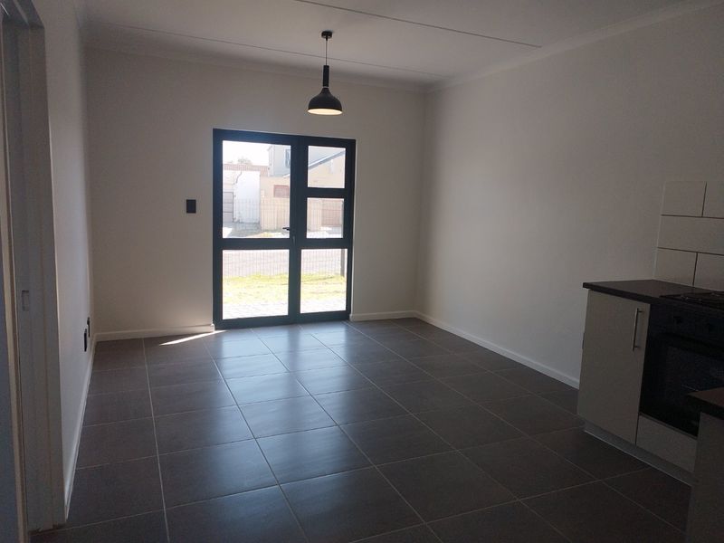 An open-plan living and kitchen area featuring modern tiled flooring, built-in kitchen cabinetry with integrated appliances, and a glass door leading to the exterior.