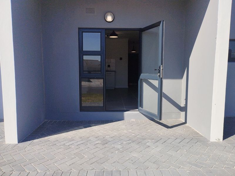 A clean, paved patio area featuring a modern aluminium framed glass door providing access to the interior of the apartment.