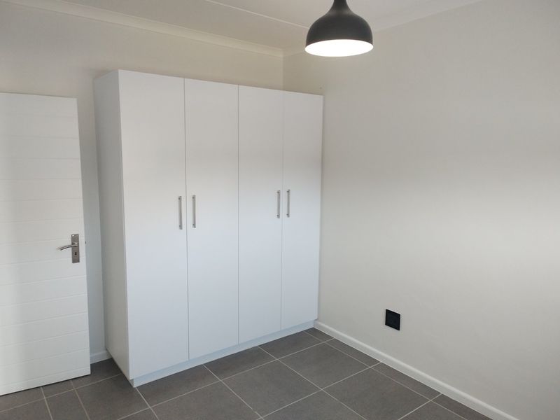 A clean, modern bedroom featuring neutral tiled flooring, crisp white walls, and a spacious built-in wardrobe with contemporary finishes.