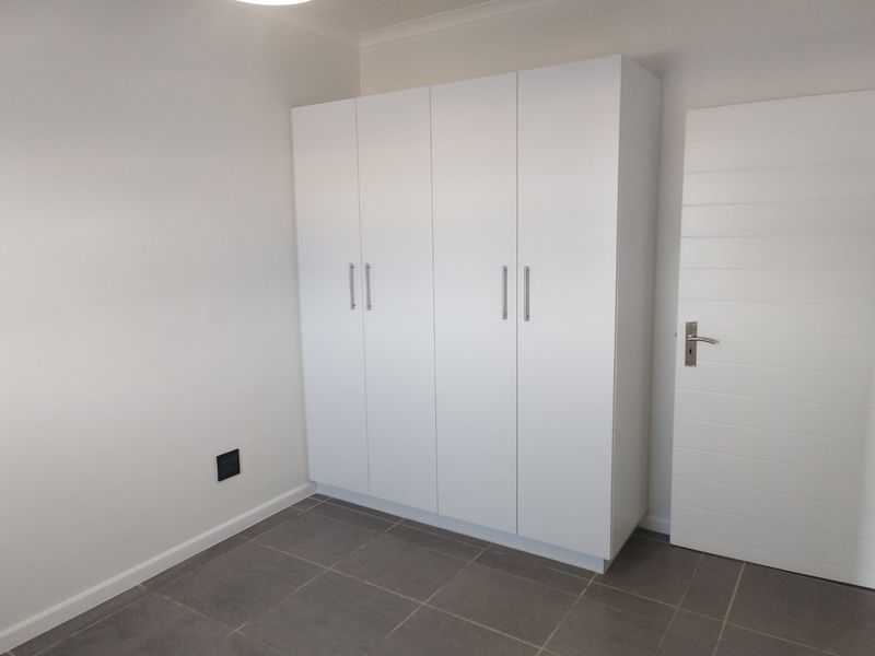 A clean, modern bedroom featuring neutral tiled flooring and a large, white built-in wardrobe with sleek handles.