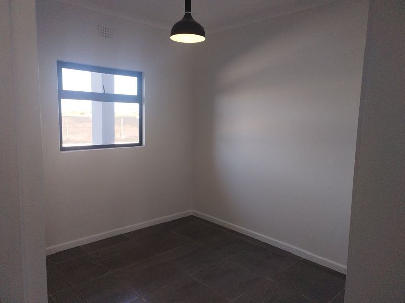 A clean, empty bedroom featuring neutral tiled flooring, a modern pendant light, and an aluminium-framed window.