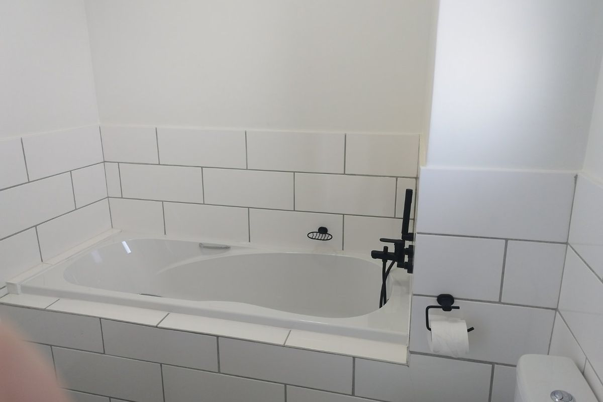 A clean, modern bathroom featuring a built-in bathtub with white subway tile surround and contemporary black matte fixtures.