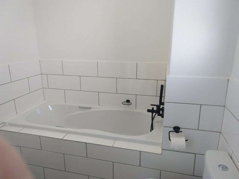 A clean, modern bathroom featuring a built-in bathtub with white subway tile surround and contemporary black matte fixtures.