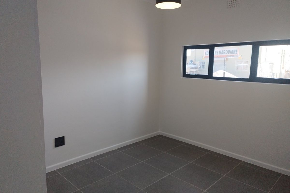 A clean, empty bedroom featuring neutral tiled flooring, a modern pendant light, and a horizontal aluminium-framed window.