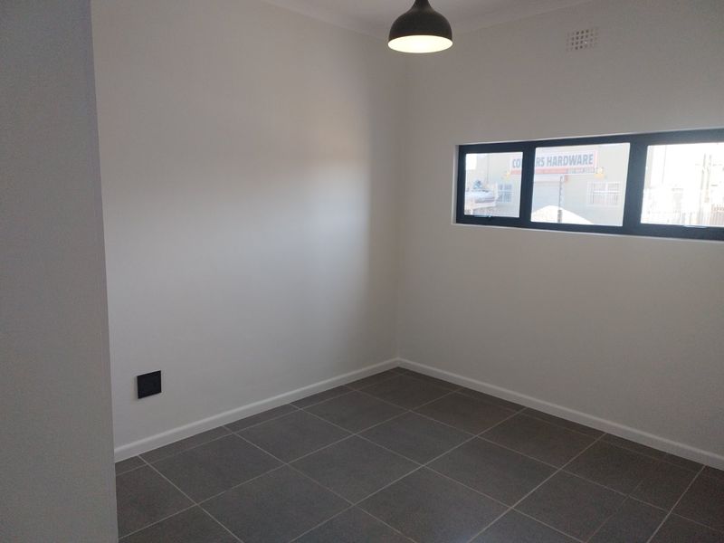 A clean, empty bedroom featuring neutral tiled flooring, a modern pendant light, and a horizontal aluminium-framed window.