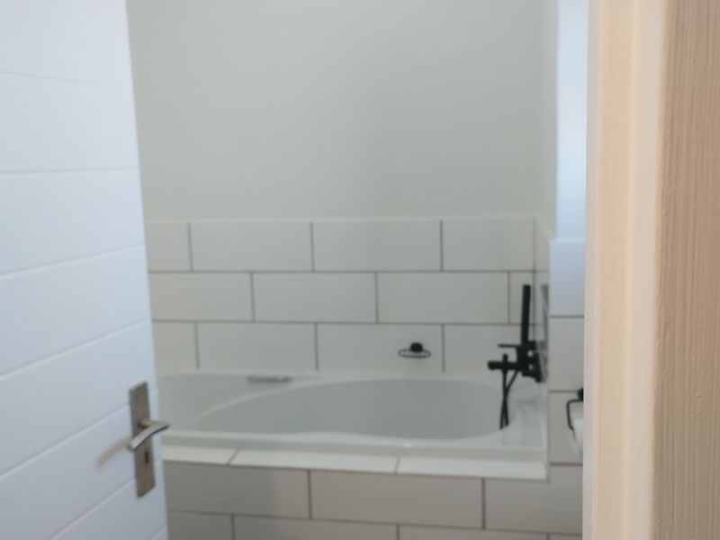 A clean, modern bathroom featuring a built-in bathtub with subway tile surround, black matte fixtures, and a white toilet.