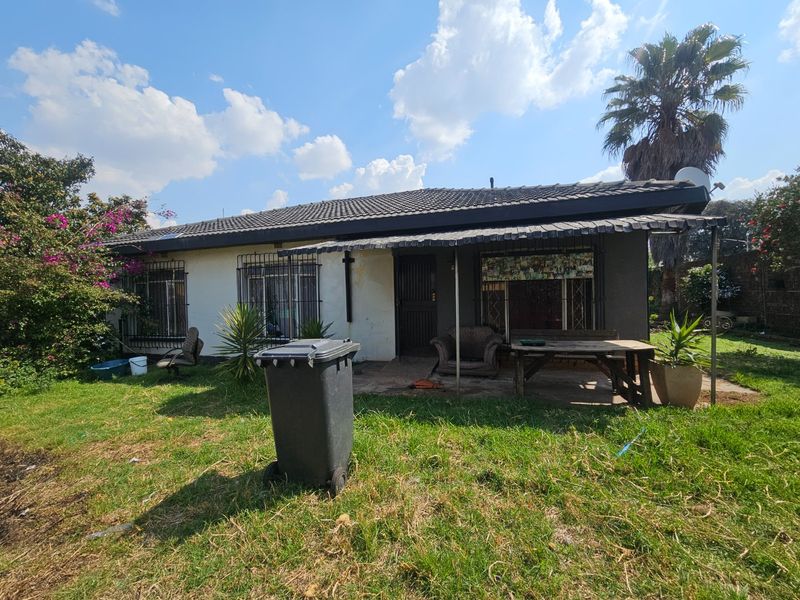 Rear view of a single-story house featuring a covered patio area, security bars on windows, and a large garden space.