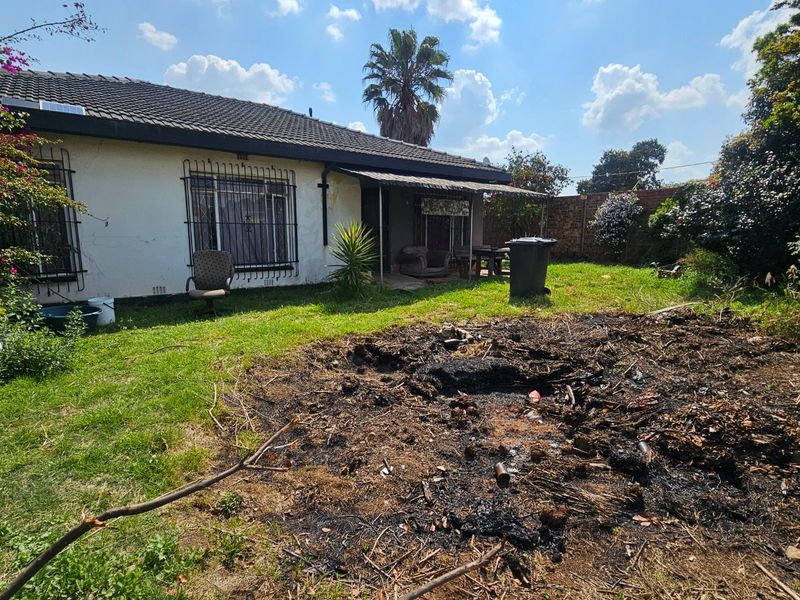 Rear view of the house featuring a covered patio, security bars on windows, and a large garden area requiring maintenance.