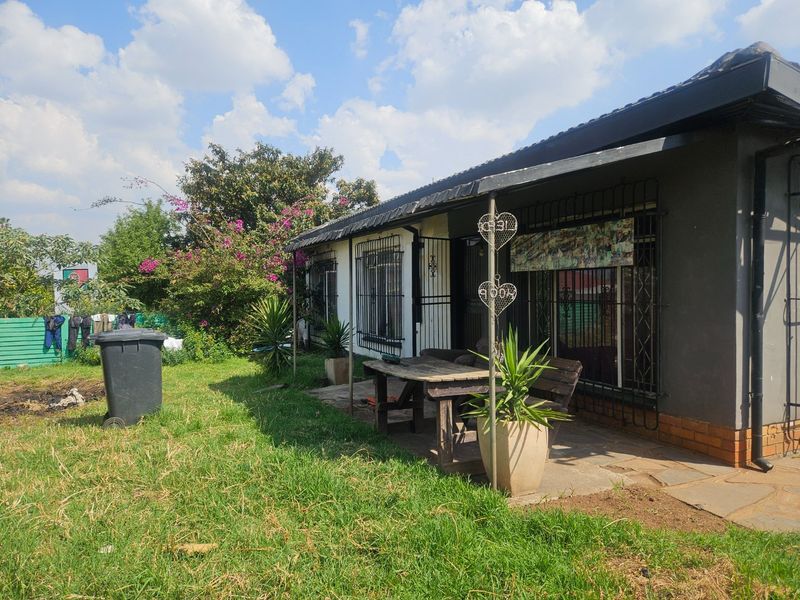 Rear exterior view of the house featuring a paved patio area, security bars on windows, and a garden space.