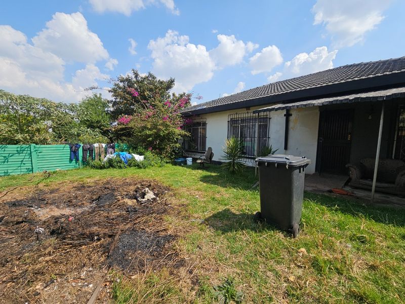 Rear exterior view of the house featuring a tiled roof, security bars on windows, and a garden area with a precast concrete boundary fence.