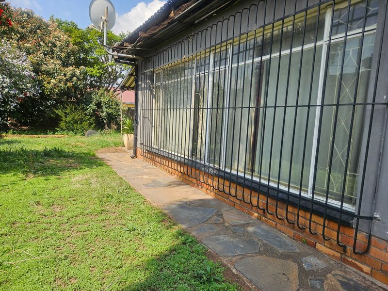 Rear exterior view of the property featuring stone paving, security bars on windows, and a satellite dish installation.