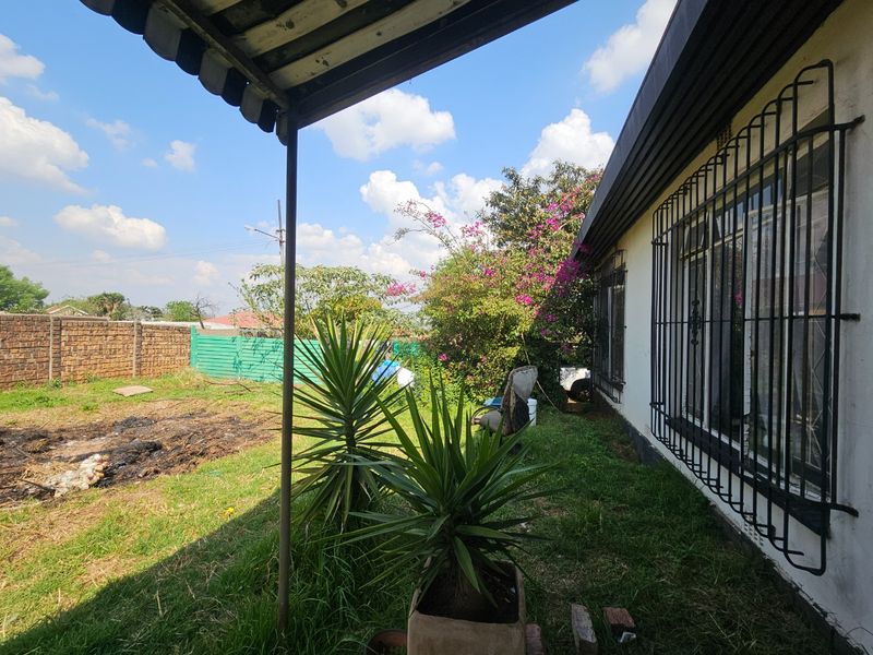 Rear exterior view showing a covered patio area, security bars on windows, and a garden space with boundary walling.