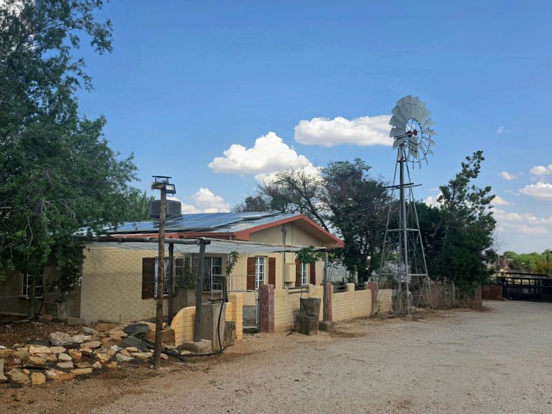 Front exterior view of a rural property featuring solar panels, a traditional windmill, and a brick boundary wall with security features.