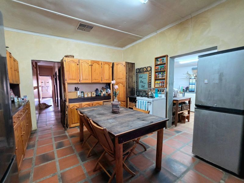 A rustic kitchen featuring traditional terracotta tile flooring and extensive wooden cabinetry, offering a functional layout with an adjacent scullery area.