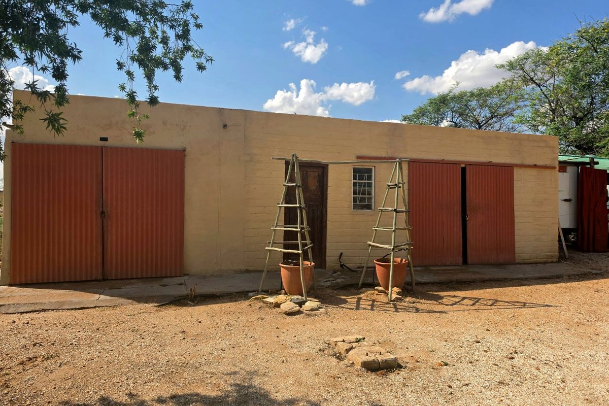Rear view of a single-story outbuilding or garage featuring corrugated metal doors, masonry walls, and a concrete apron.