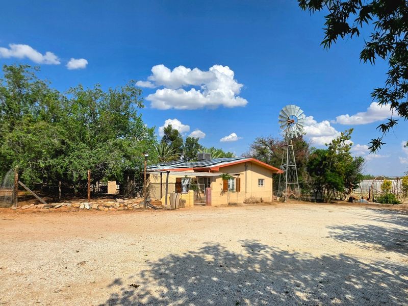 Front view of a rural property featuring a gravel driveway, solar panel installation on the roof, and a traditional windmill structure.