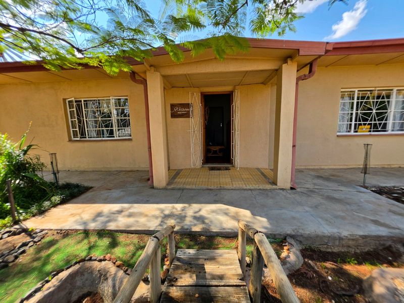 Front entrance of the house featuring a covered porch, security gates, and a small wooden footbridge leading to the concrete patio area.