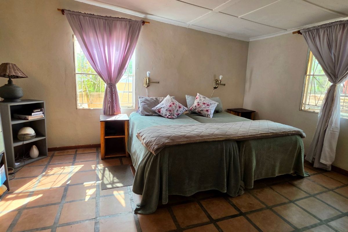 A bedroom featuring tiled flooring, wall-mounted reading lights, and dual windows. The room requires cosmetic updates to the ceiling and wall finishes.