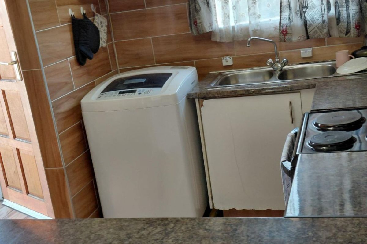 A functional kitchen area featuring laminate countertops, a double sink, tiled splashbacks, and built-in cabinetry with some visible wear to the base units.