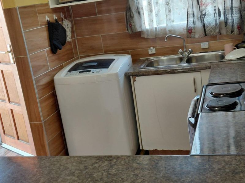 A functional kitchen area featuring laminate countertops, a double sink, tiled splashbacks, and built-in cabinetry with some visible wear to the base units.