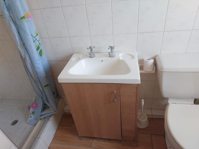 A functional bathroom featuring a vanity basin, toilet, and shower enclosure with tiled finishes, currently showing signs of wear and dated fixtures.