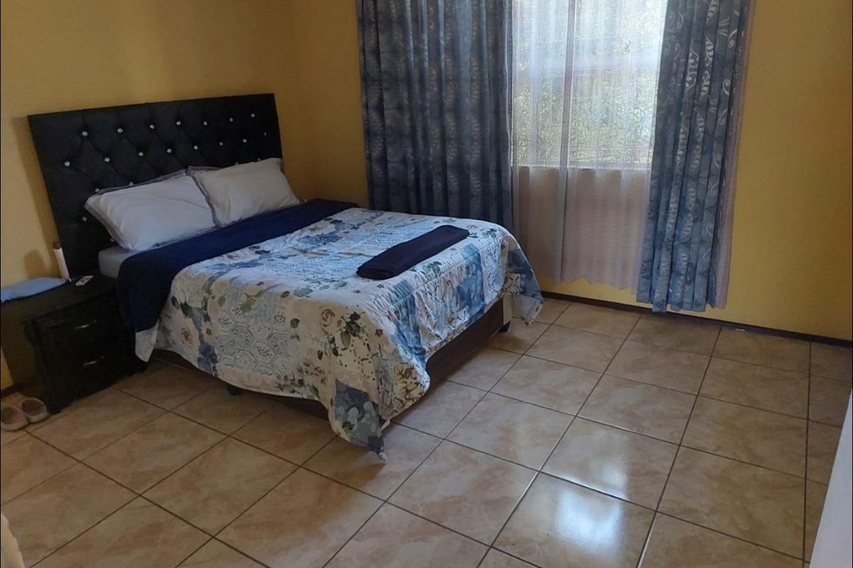 A bedroom featuring tiled flooring and large windows with curtain rails, providing a functional and neutral living space.