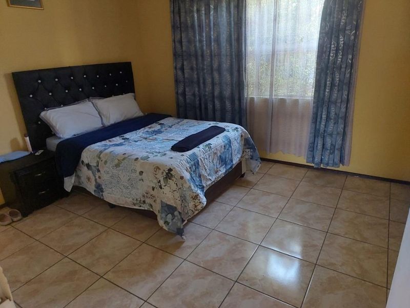 A bedroom featuring tiled flooring and large windows with curtain rails, providing a functional and neutral living space.