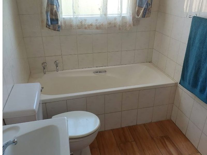 A functional bathroom featuring a built-in bathtub, pedestal washbasin, toilet, and wood-look floor tiles with partial wall tiling.