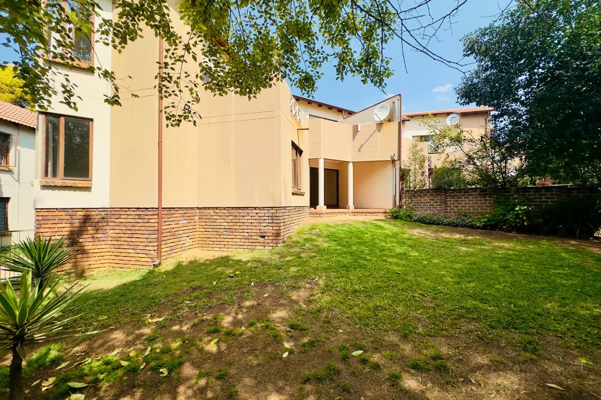 Rear view of the apartment building featuring a private garden, brick boundary wall, and a covered patio area.