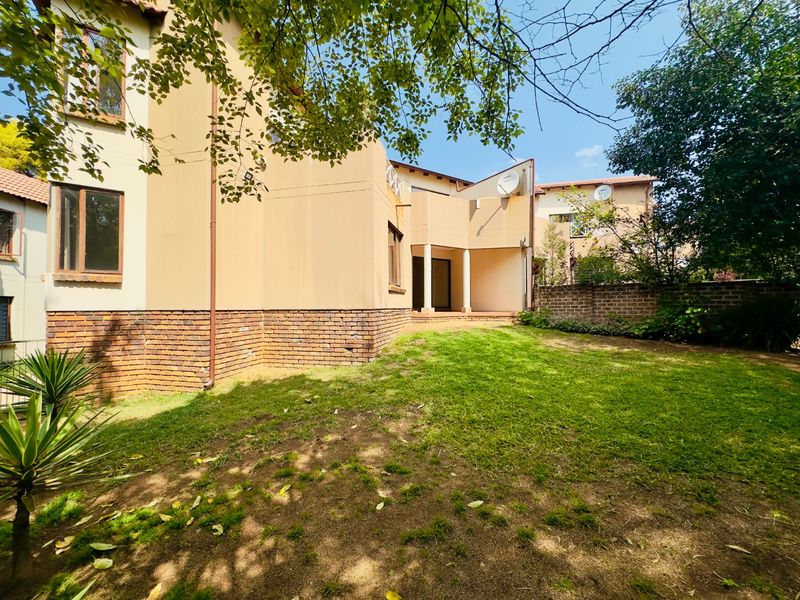 Rear view of the apartment building featuring a private garden, brick boundary wall, and a covered patio area.