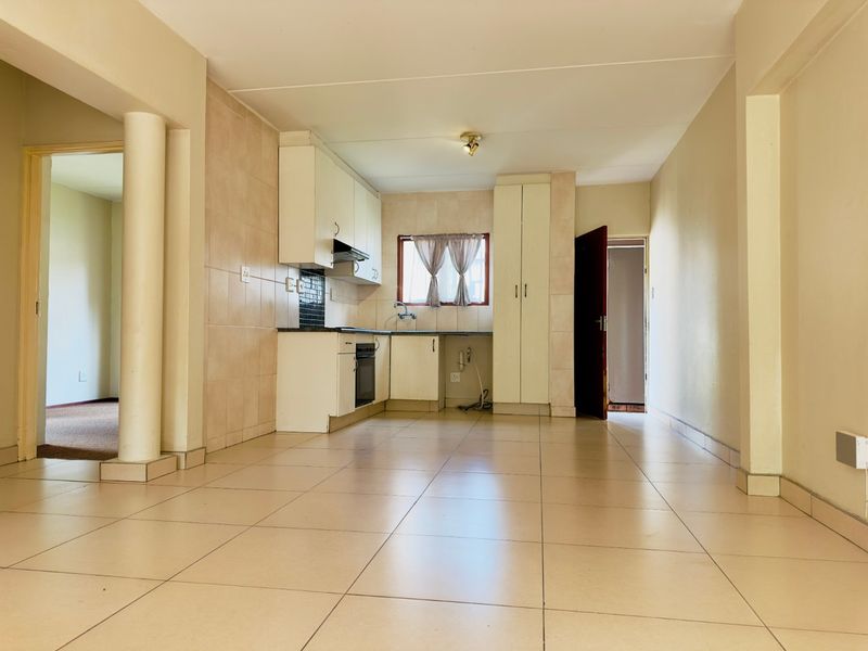 Open-plan kitchen and living area featuring tiled flooring, built-in cabinetry, and integrated cooking appliances in a neutral, functional layout.