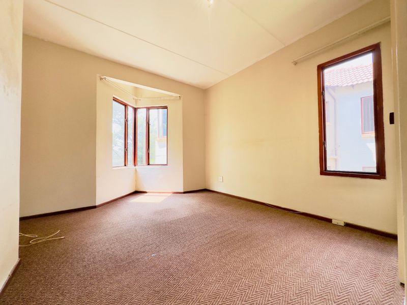 An empty bedroom featuring a bay window, timber frames, and carpeted flooring, offering a blank canvas for potential interior design updates.