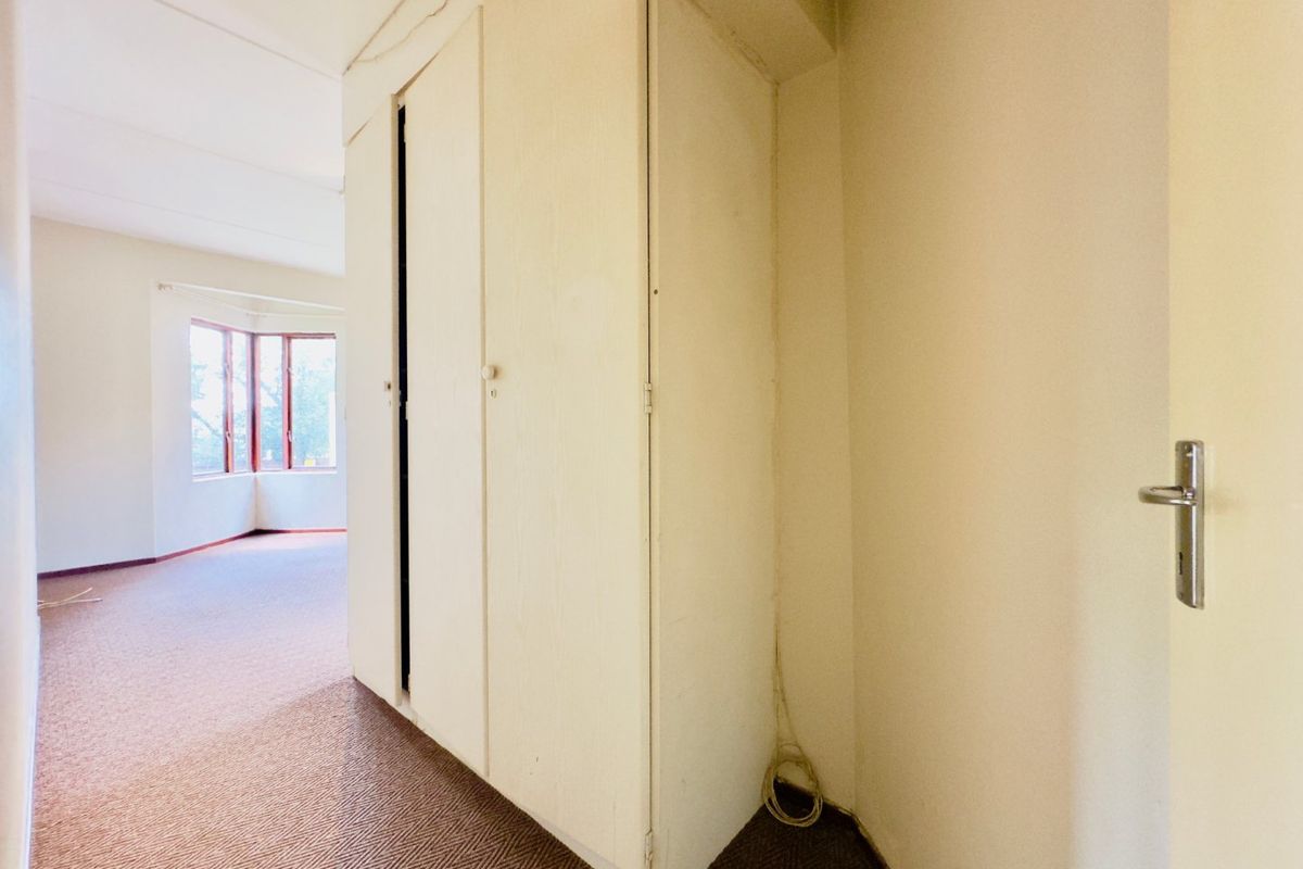 An empty bedroom featuring built-in cupboards, carpeted flooring, and a bay window, offering a blank canvas for renovation.