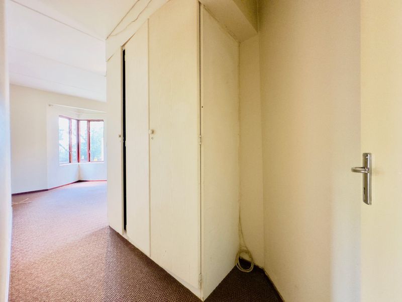 An empty bedroom featuring built-in cupboards, carpeted flooring, and a bay window, offering a blank canvas for renovation.
