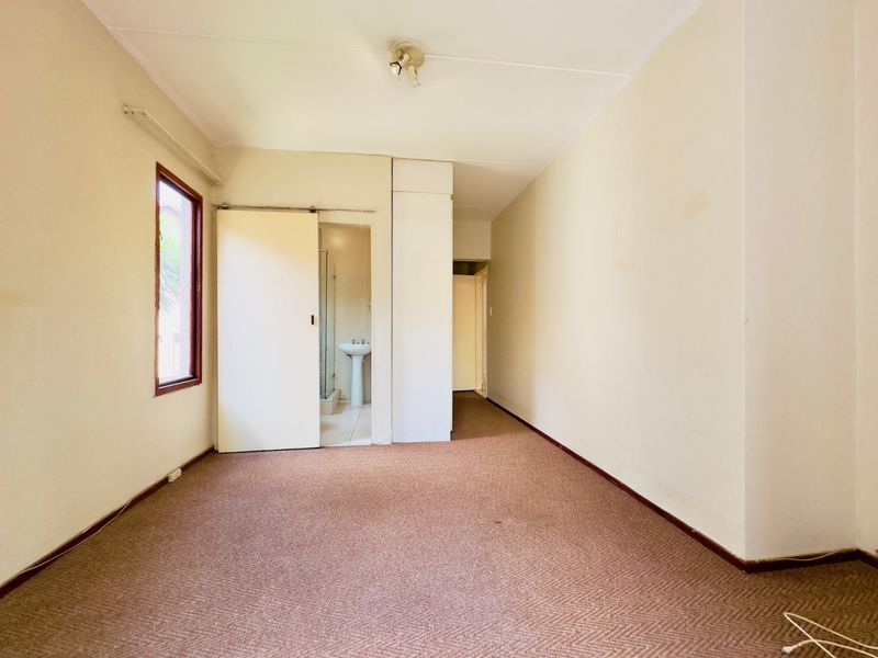 An empty bedroom featuring carpeted flooring, a built-in cupboard, and direct access to an en-suite bathroom.
